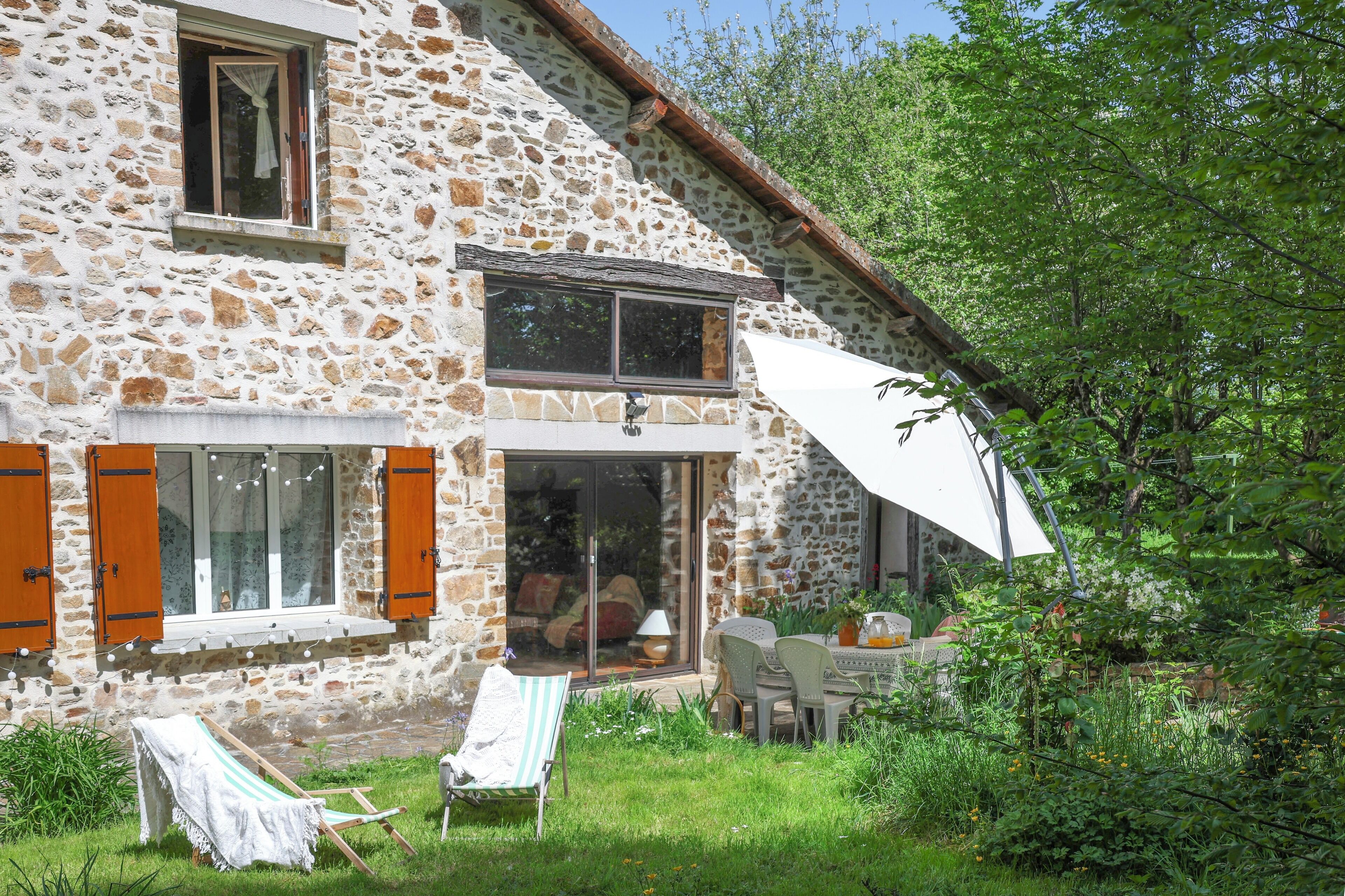 A stone house with a patio, outdoor seating, and a large umbrella.