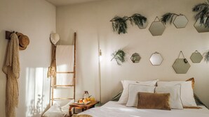 Une chambre à coucher bien rangée, avec un lit, des oreillers, une table de chevet sur laquelle se trouve un panier de fruits et des boissons, un panier suspendu et un porte-serviettes fixé au mur.