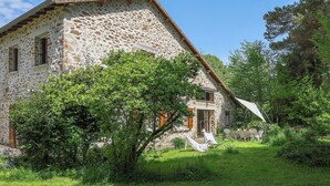 Une maison en pierre avec un toit en pente, un petit porche et un jardin agrémenté d’une table et de chaises.