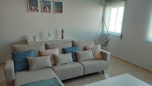 Un salon moderne avec un canapé d’angle beige, une table basse blanche et un fauteuil suspendu. Trois tableaux encadrés sont accrochés au mur, au-dessus du canapé.
