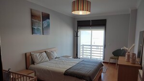 Une chambre à coucher comprenant un lit, un bureau, une chaise, une lampe sur pied et des œuvres d’art accrochées au mur.