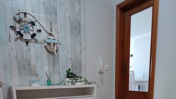 Une pièce avec une console blanche, un élément décoratif mural, une porte en bois et un tapis à motifs.