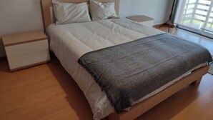Un lit bien fait, avec une couverture grise, une tête de lit en bois et du linge de lit blanc.