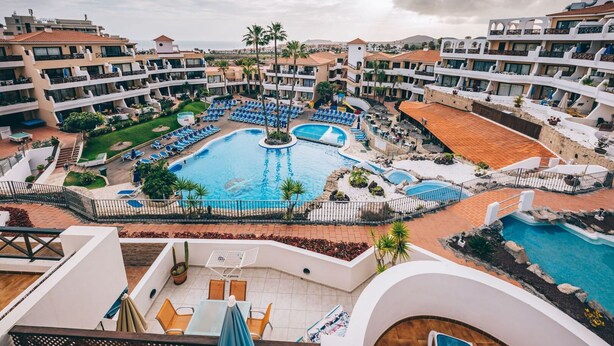 Ett semesterhotell med flera pooler, solstolar och utsikt över det omgivande landskapet.
