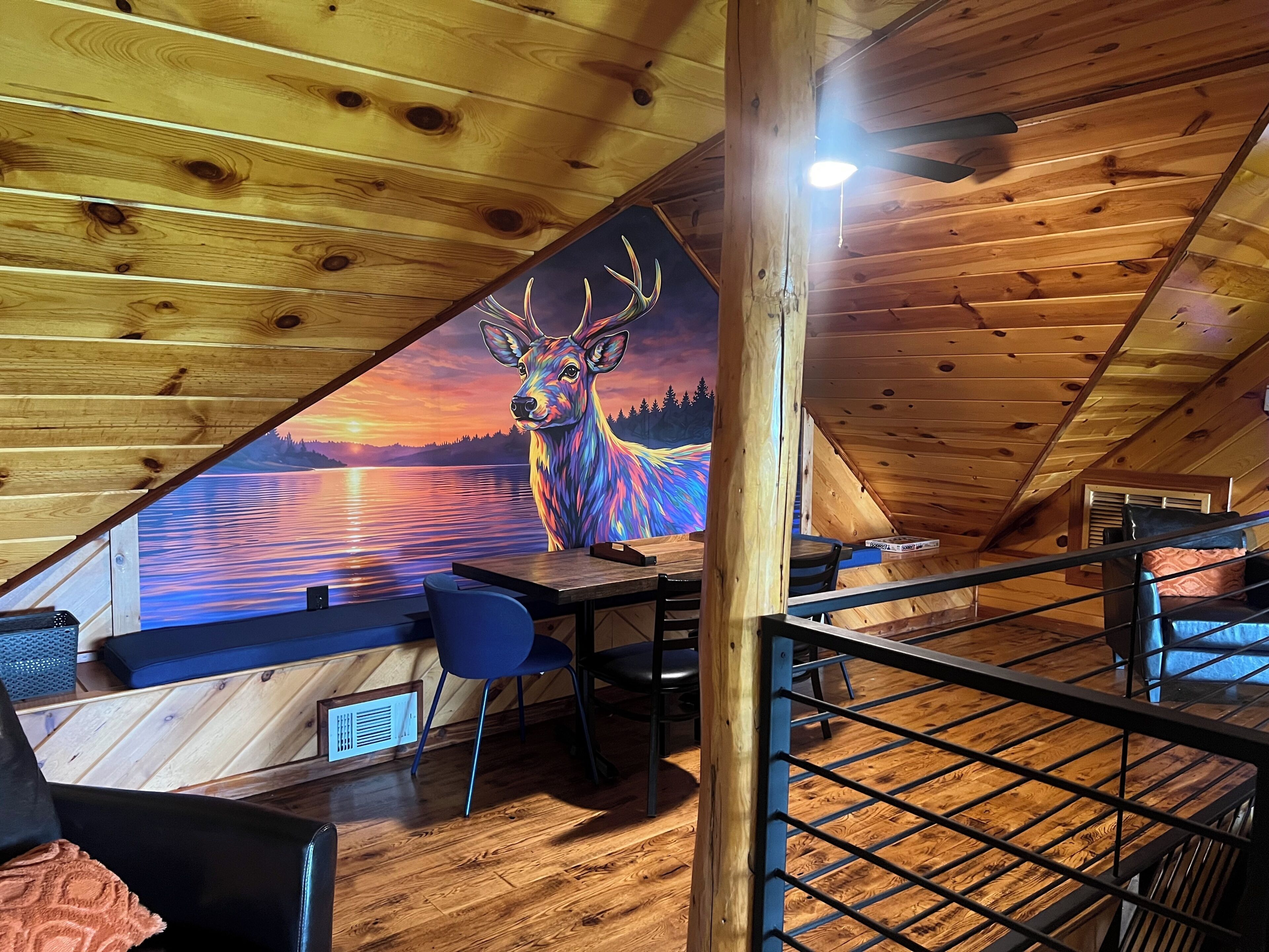 An attic room with a wooden ceiling, a table, chairs, and a mural of a deer.