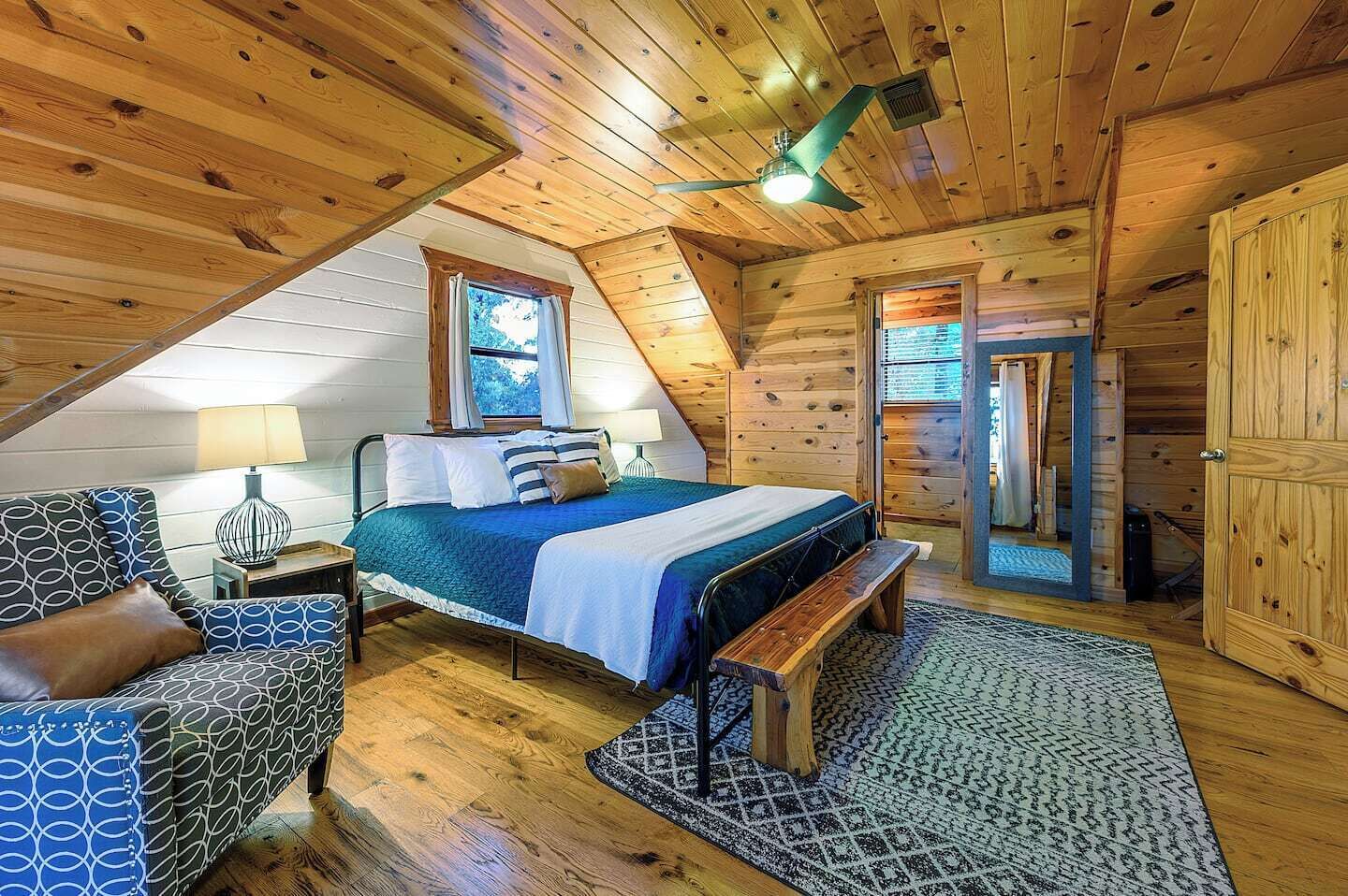A cozy attic bedroom with a bed, a bench, a chair, and a wooden door.