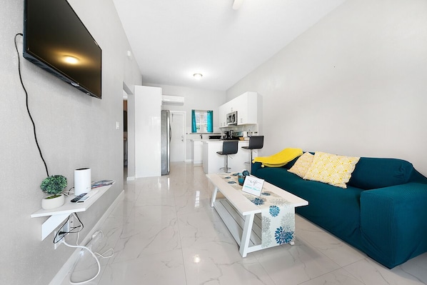 Een moderne woonkamer met een flatscreen televisie, een salontafel, een bank en een keuken op de achtergrond.