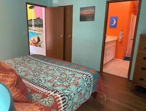 Un dormitorio con cama, armario y baño visible a través de una puerta abierta.