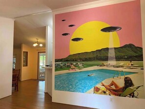 Habitación con un amplio mural de una escena de piscina, suelo de madera y una puerta que da a otra estancia.
