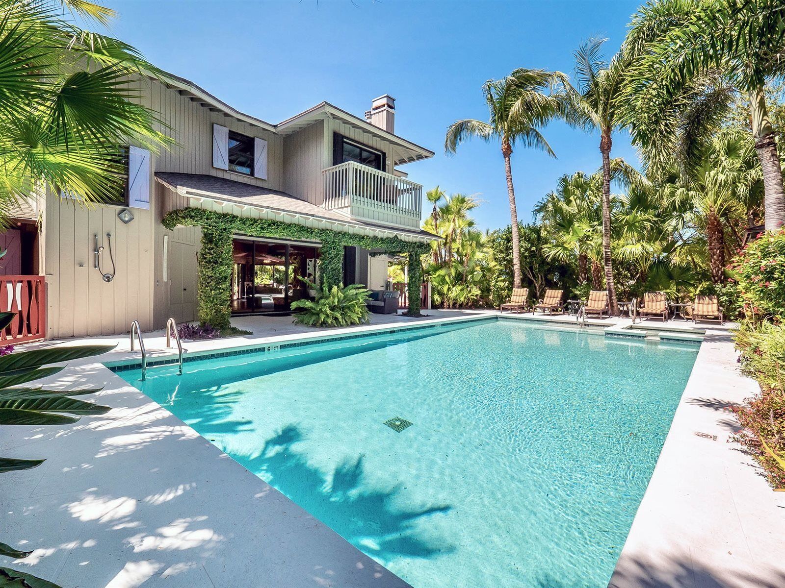 A two-story house with a swimming pool, surrounded by palm trees and a covered patio area.