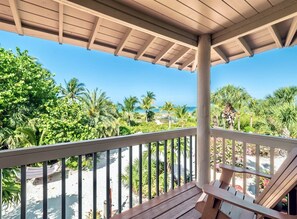 A wooden deck with a railing overlooking a beach, palm trees, and a clear blue sky. - Bali Hi Estate (Captiva)