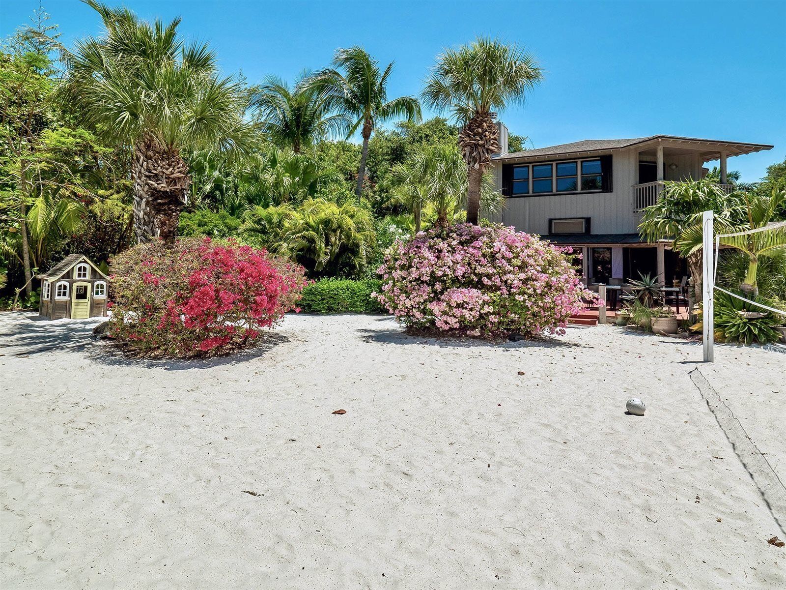 Une propriété située en bord de mer, comprenant une maison à deux étages, un petit abri pour bateaux et une végétation tropicale luxuriante.