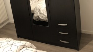 A dark-colored wardrobe with a mirror, a bed with patterned bedding, and a wooden floor. - Chambre Simple Privée -saint Priest (Saint-Priest)