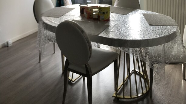 A dining area with a round table, four chairs, and a window with curtains. There are cans and a box on the table. - Chambre Simple Privée -saint Priest (Saint-Priest)