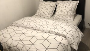 A bed with a geometric patterned bedspread and pillows, a dark headboard, and a small framed picture on the wall. - Chambre Simple Privée -saint Priest (Saint-Priest)