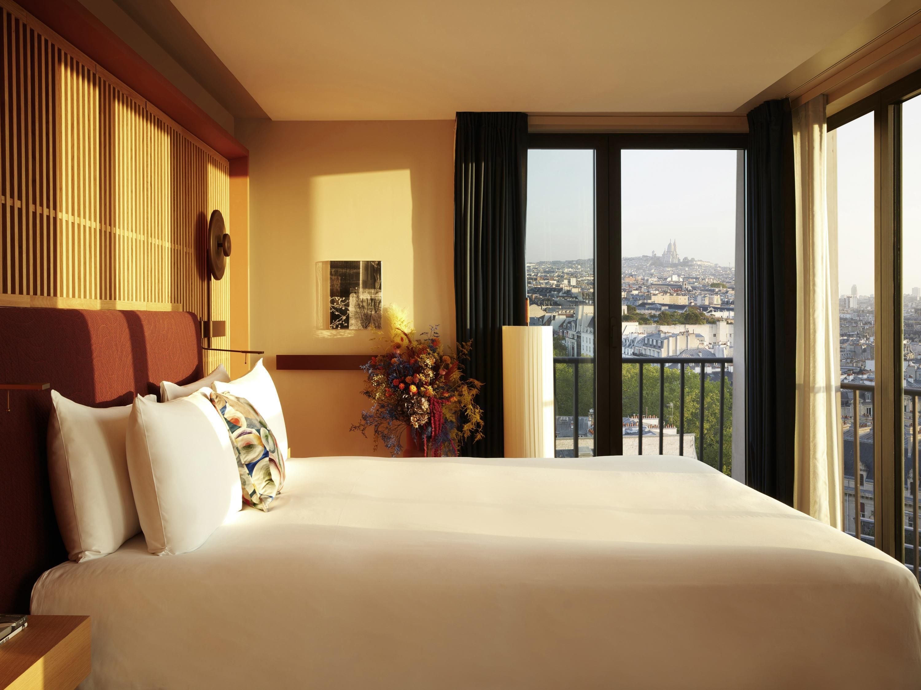 A hotel room with a large bed, a view of the city, and a decorative vase on the nightstand.