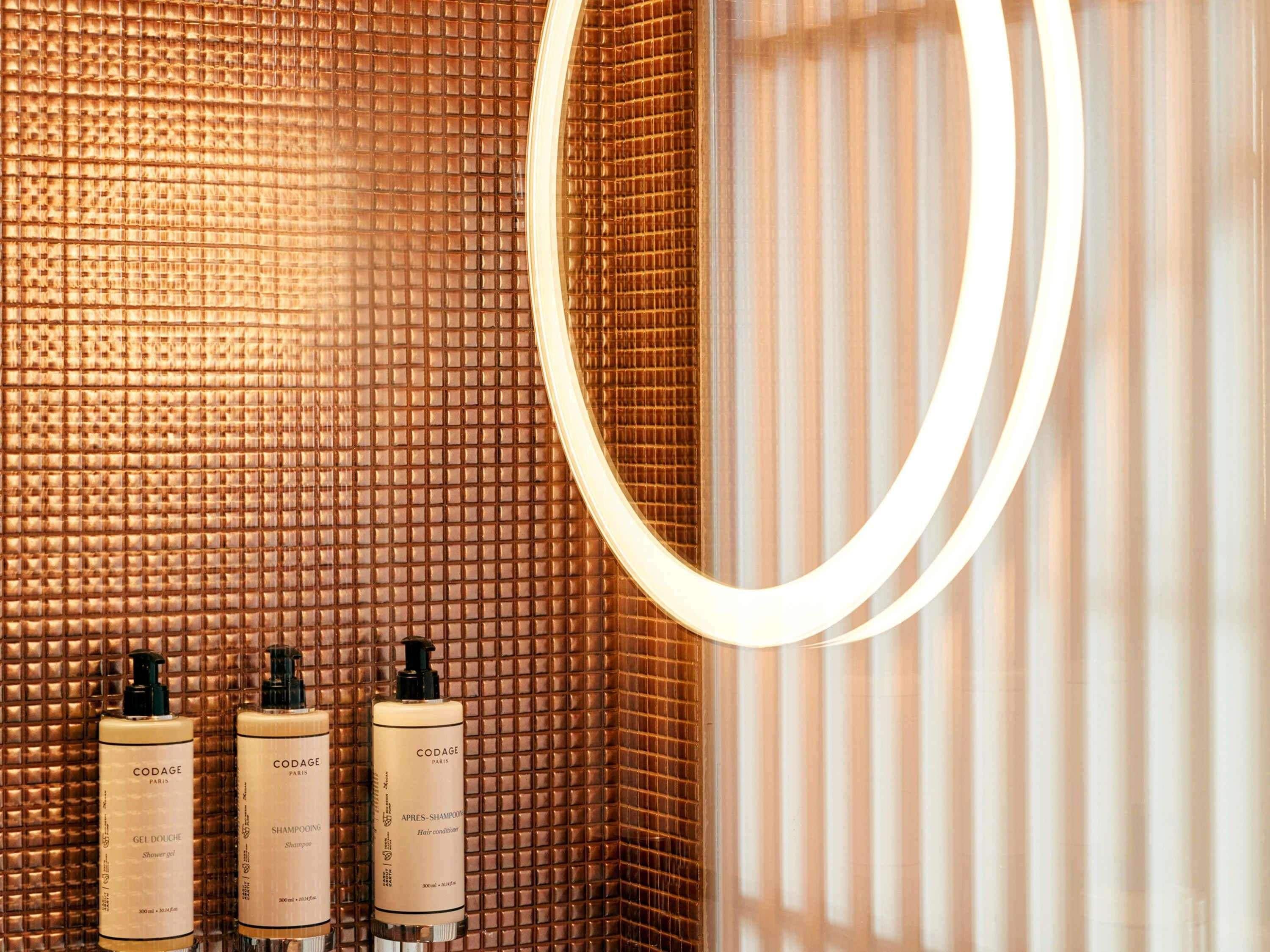Un baño con pared texturizada, un espejo y tres botellas de productos para el cabello CODAGE Paris.