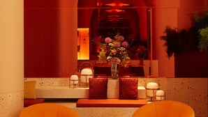 A lobby with two orange bean bag chairs, a central table with a vase of flowers, and a reception desk with a mirror.