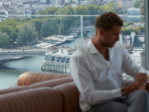 A person sitting on a couch with a city view through a window.