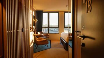 A hotel room with a bed, a desk, a chair, a wardrobe, and a view of the city.
