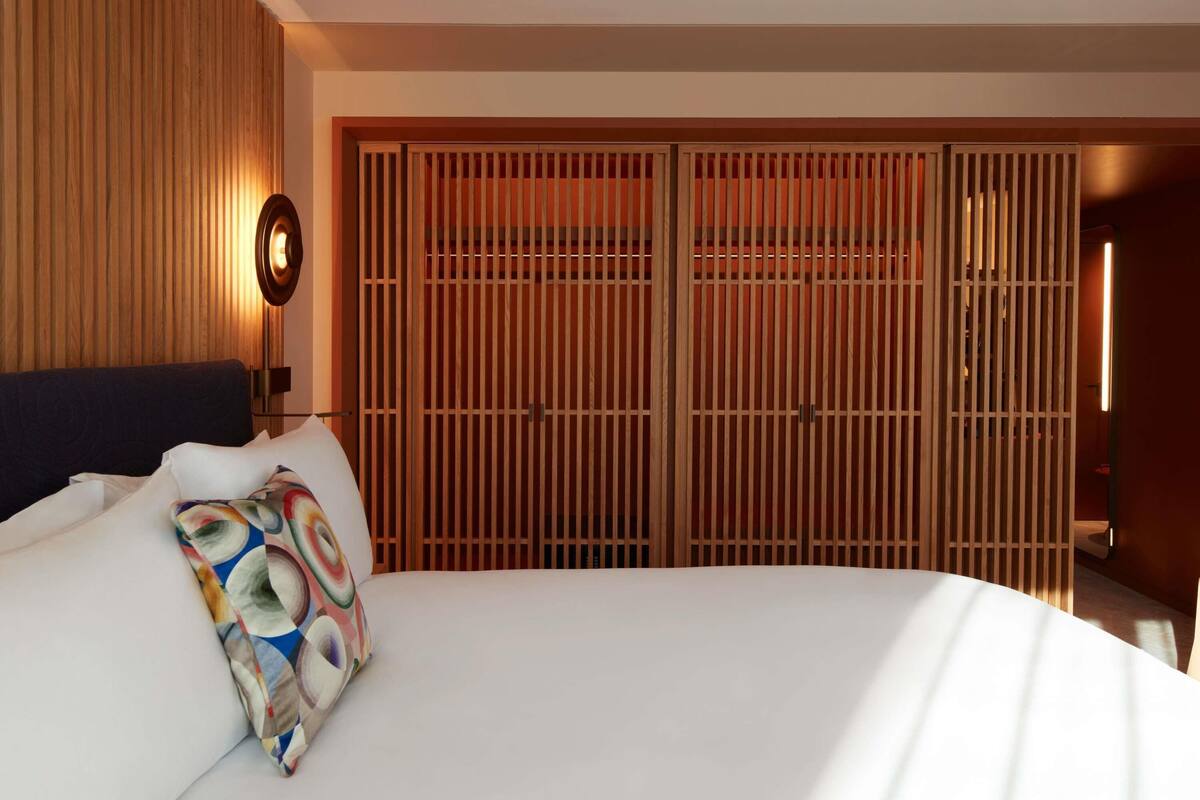 A hotel room with a large bed, a wooden wardrobe, and a wall-mounted light fixture.