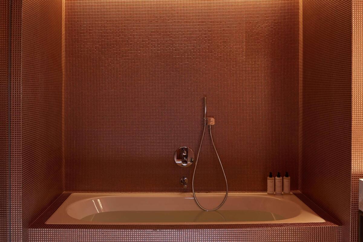A modern bathroom with a freestanding bathtub, a handheld showerhead, and a set of toiletries on the side.
