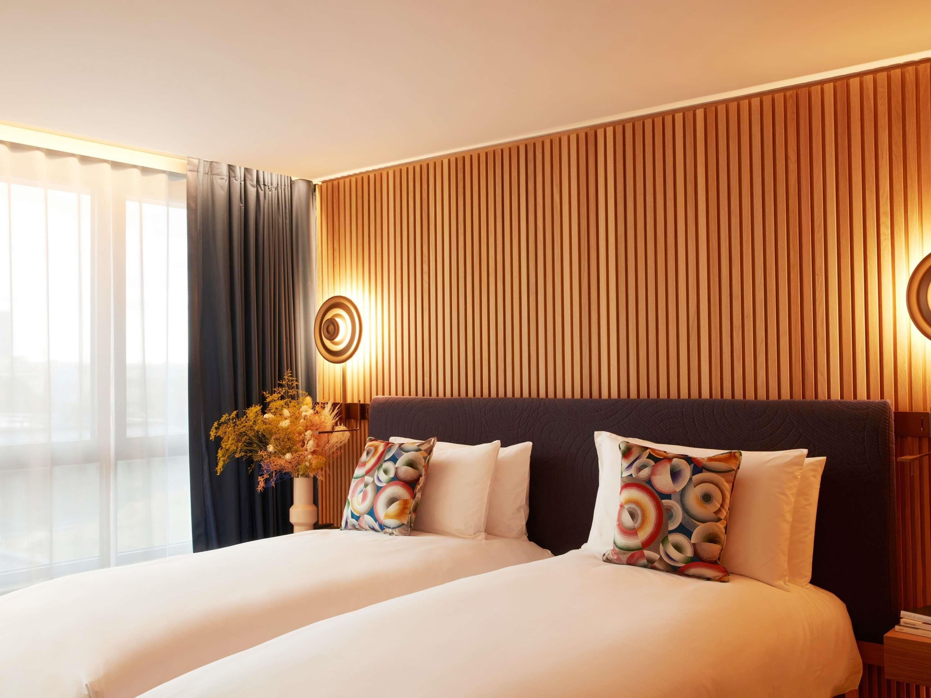 Una habitación de hotel con una cama grande, un panel de pared de listones de madera y una ventana con cortinas.