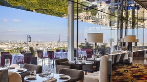 A restaurant with tables set for dining, large windows offering a city view, and a patterned carpet. - SO/ Paris Hotel (Paris)