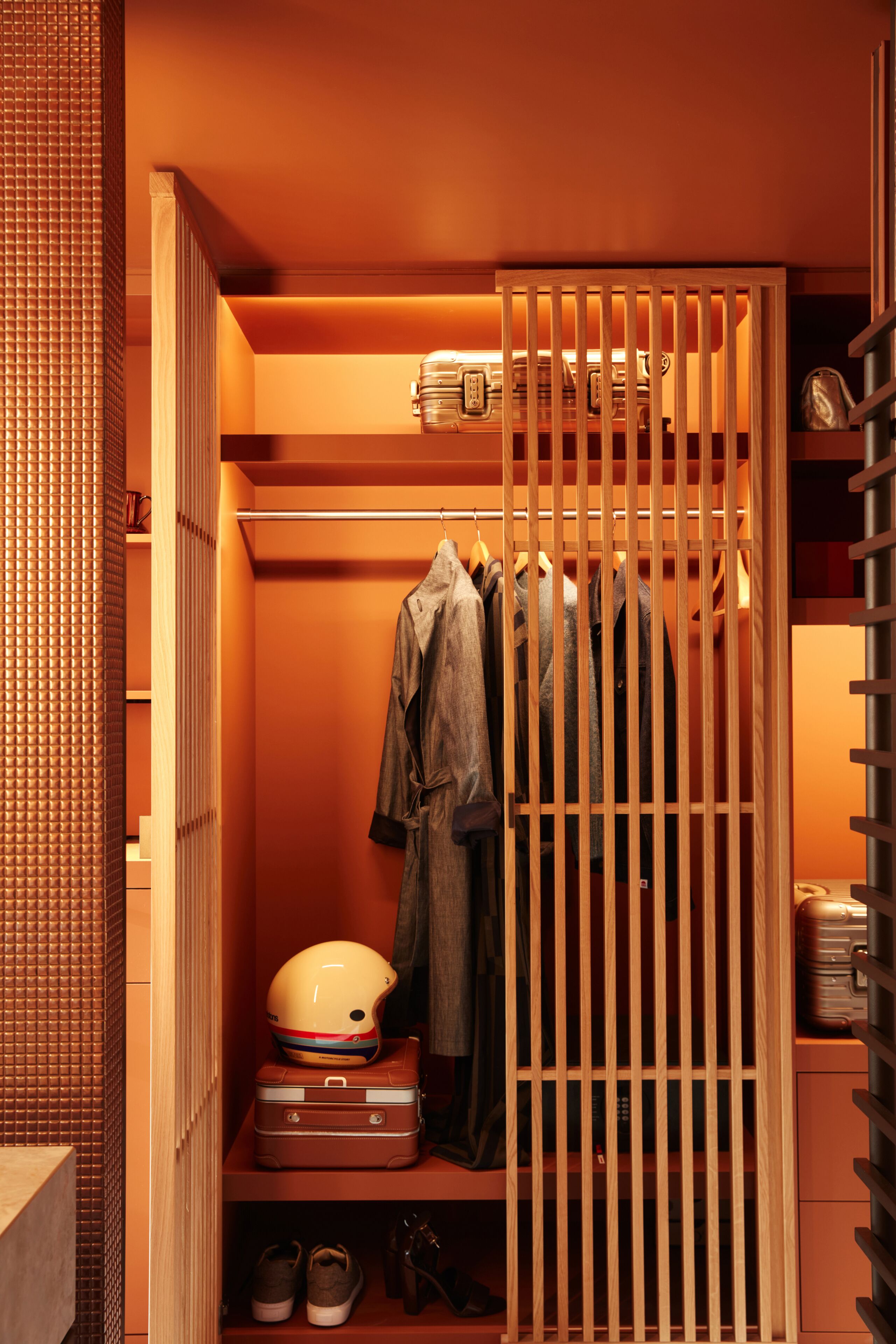 A walk-in closet with a wooden partition, shelves with clothes, a suitcase, and a helmet.