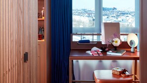 A room with a desk, a window with a city view, a blue curtain, and a wooden wardrobe.