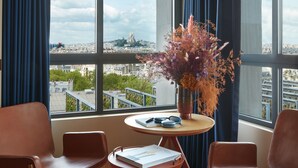 A modern room with a large window, two brown chairs, a small round table, and a vase with flowers. - SO/ Paris Hotel (Paris)