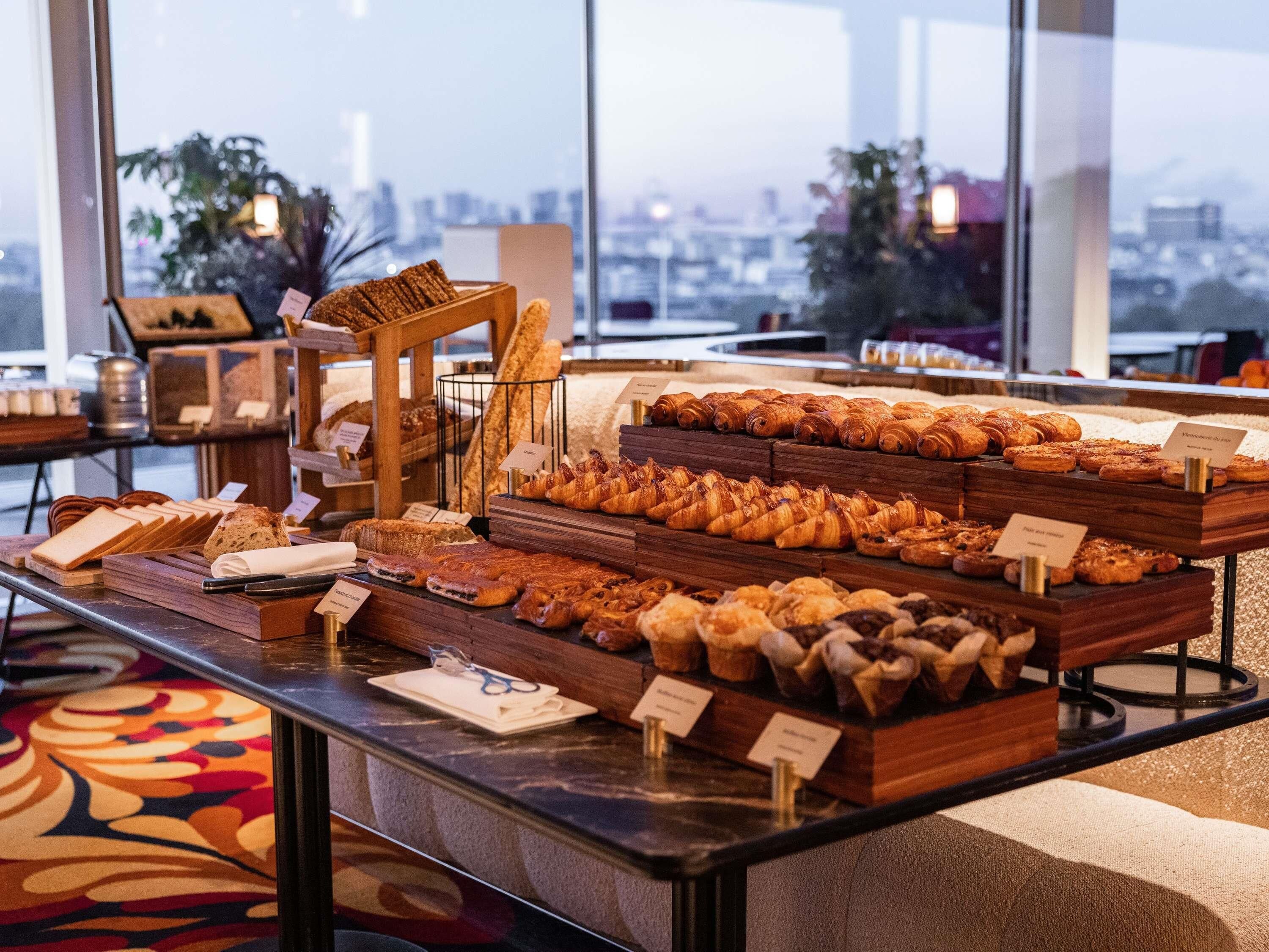 Une vitrine de boulangerie présentant diverses pâtisseries, avec une vue sur la ville en arrière-plan.