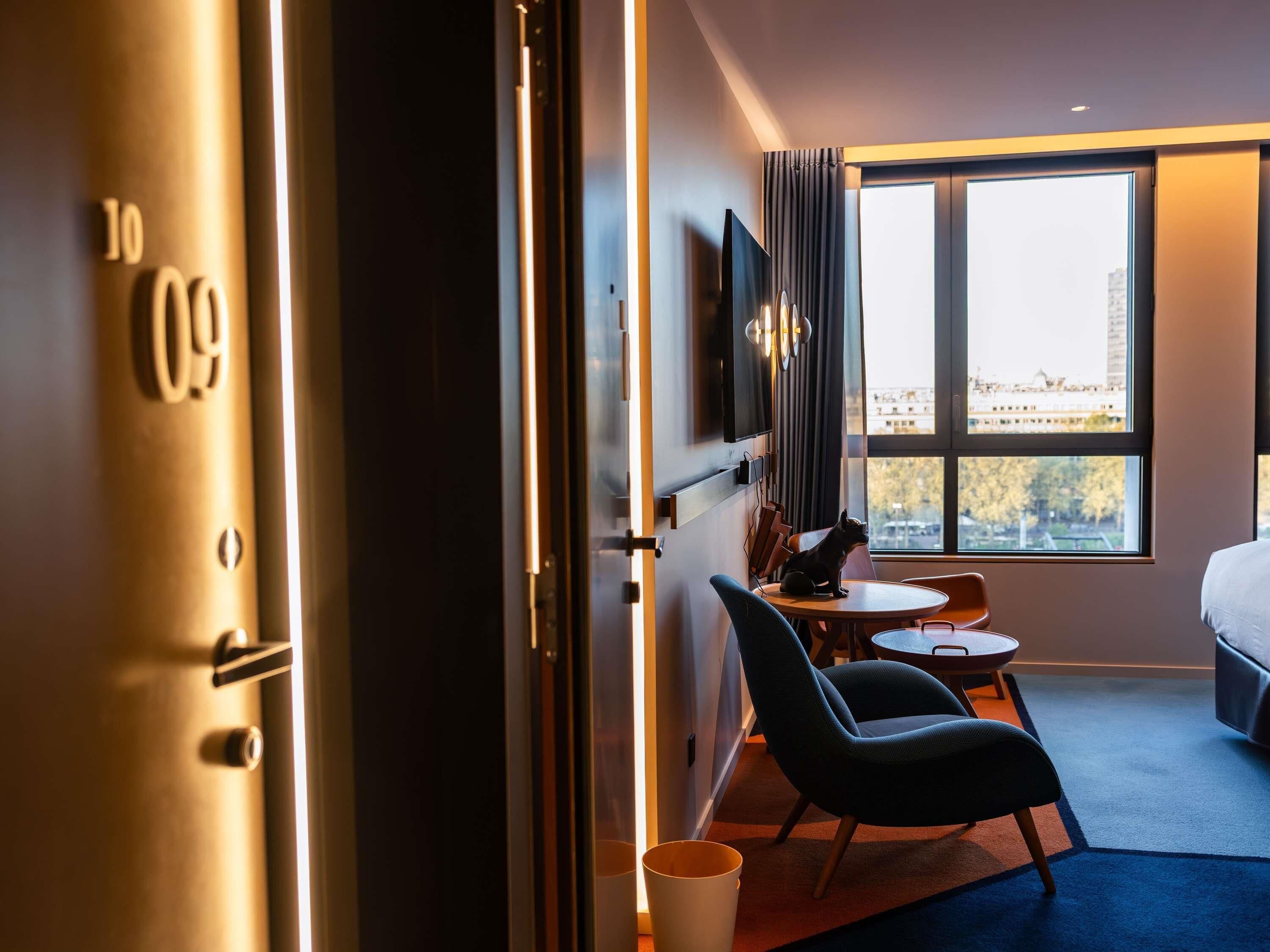 Habitación de hotel con cama, escritorio, silla, televisor y ventana con vista a la ciudad.