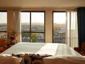A hotel room with a large bed, two windows with curtains, a vase with flowers, and a view of a cityscape. - SO/ Paris Hotel (Paris)