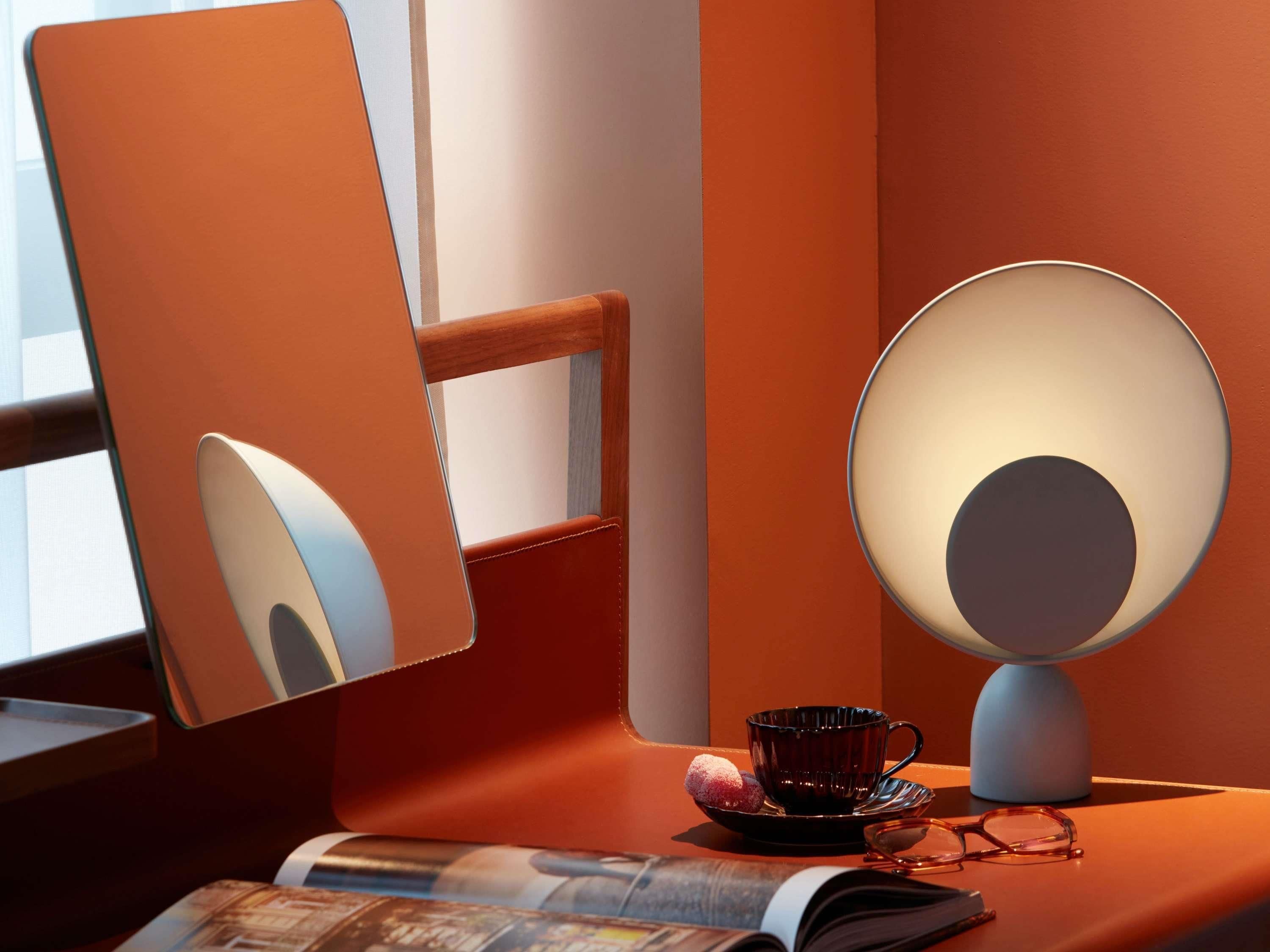A desk with a lamp, a cup, a pair of glasses, and a magazine.