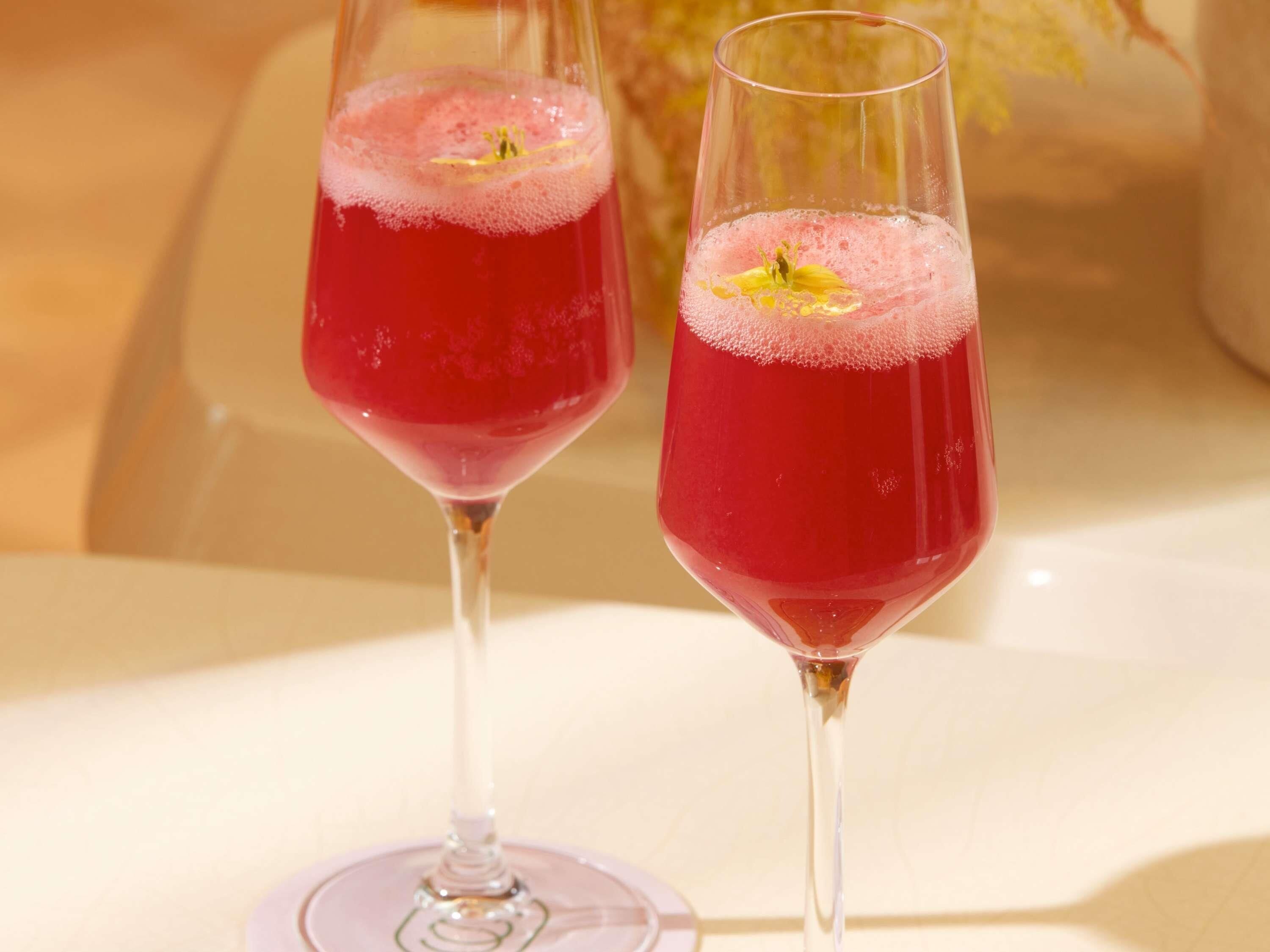 Dos vasos de bebida roja con una espuma arriba y una flor amarilla como adorno.