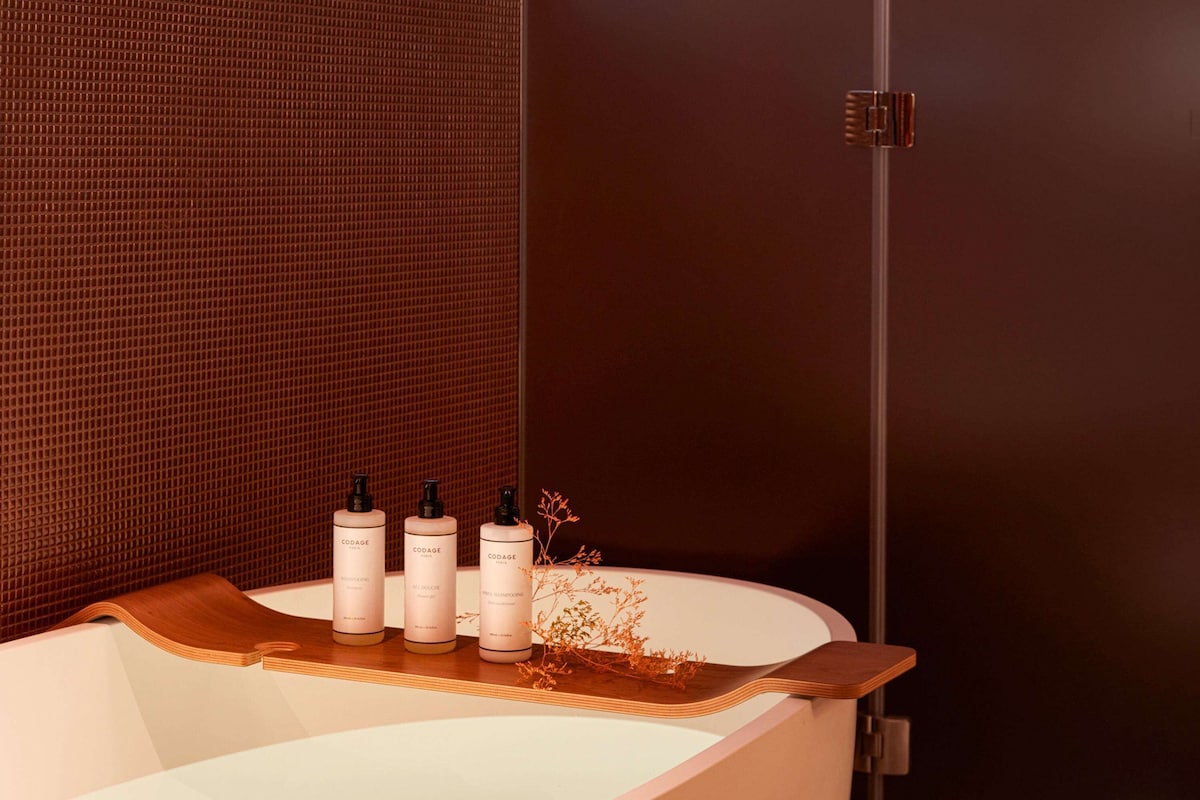 A modern bathroom with a freestanding bathtub, three bottles of Codage Paris shampoo, and a decorative plant.