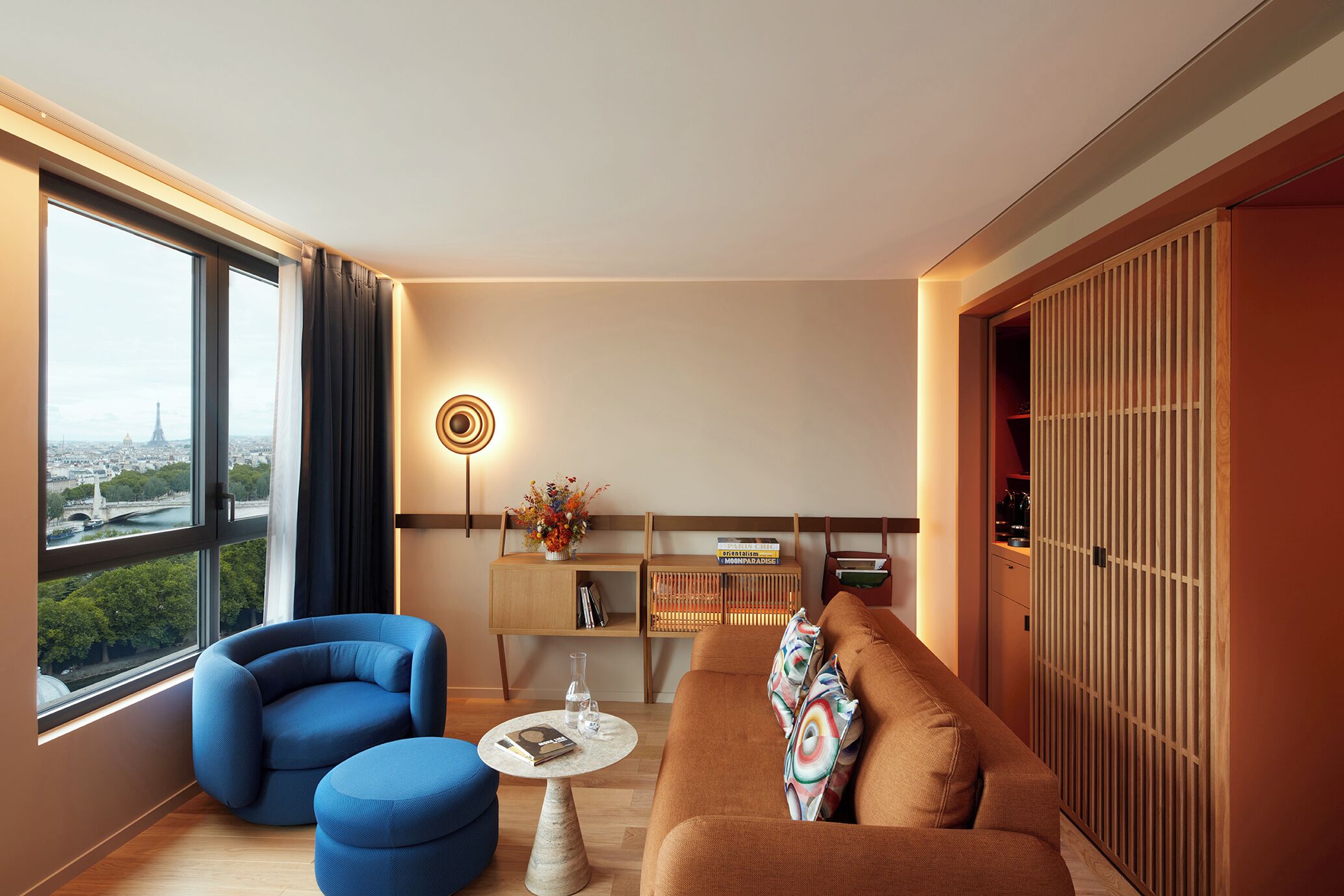 Uma sala de estar moderna com sofá, poltrona e mesa de centro, estante de livros e vista para a cidade.