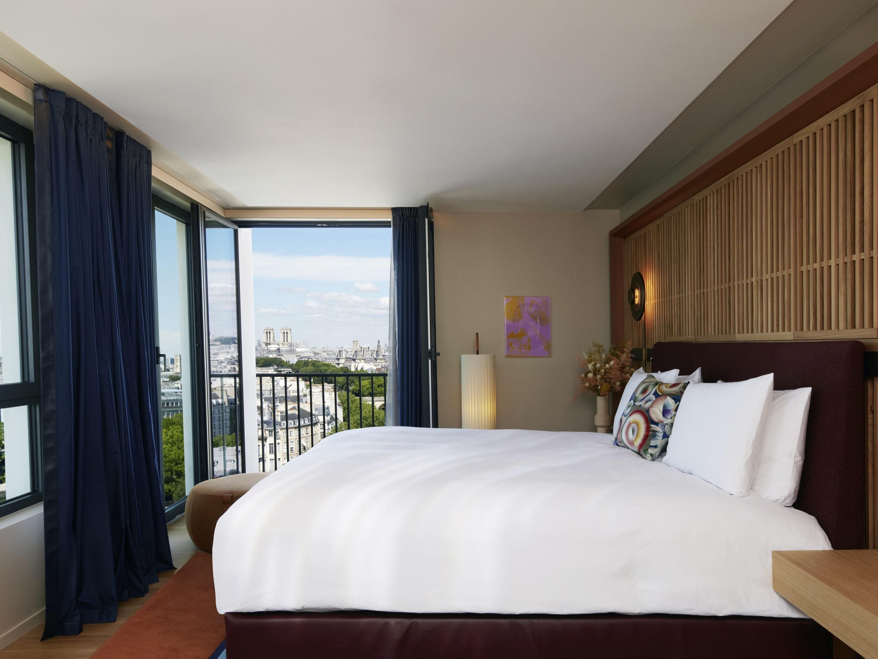 A hotel room with a large bed, a view of the city, and a balcony.