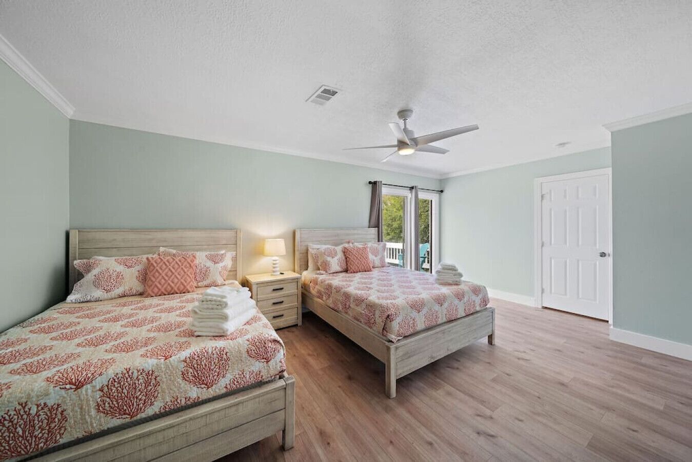 A bedroom with two beds, a ceiling fan, and a view to the outside.