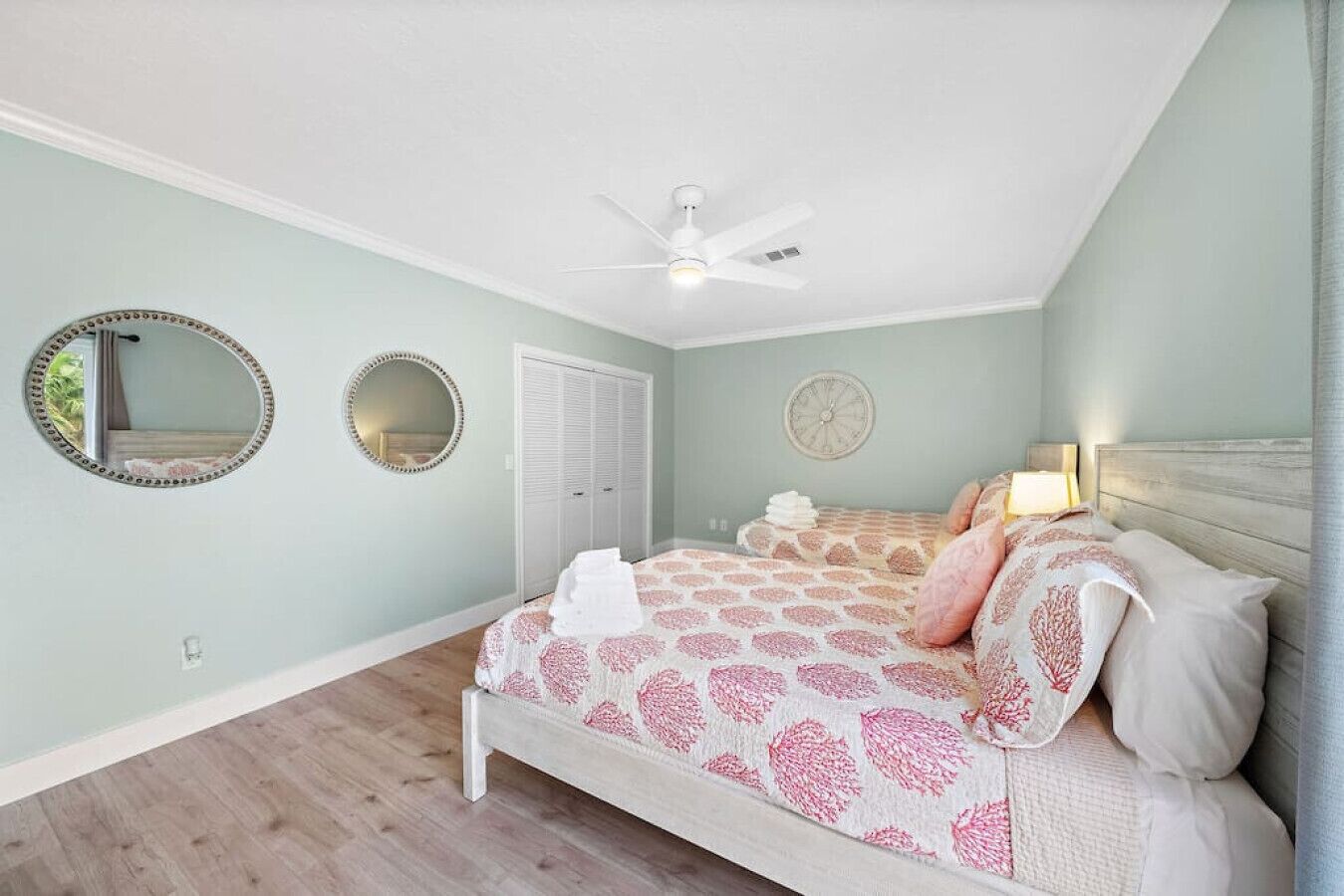 A bedroom with a bed, two round mirrors, a ceiling fan, a door, and a wall clock.
