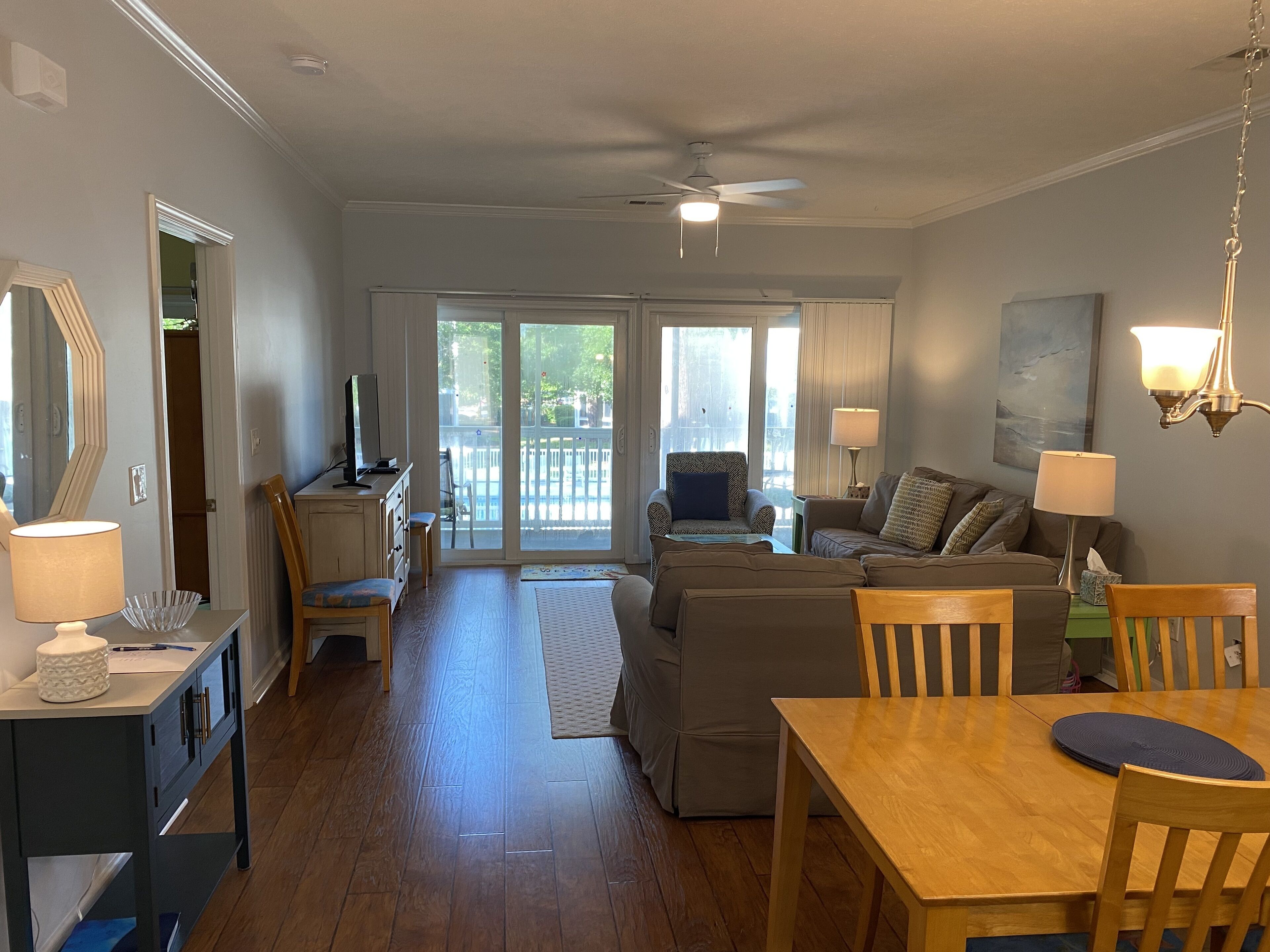 A spacious living room with a wooden dining table, a sofa set, and a television on a stand.