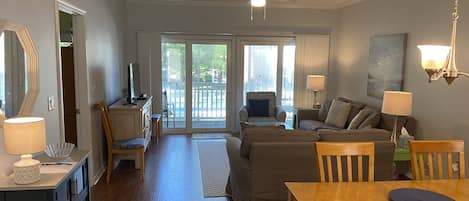 A spacious living room with a wooden dining table, a sofa set, and a television on a stand.