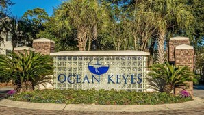 A sign for Ocean Keyes with a logo, surrounded by greenery and brick structures. - Ocean Keyes 3 BR Condo, XL balcony, pool, 1 block to beach, food,  & famous OD (North Myrtle Beach)