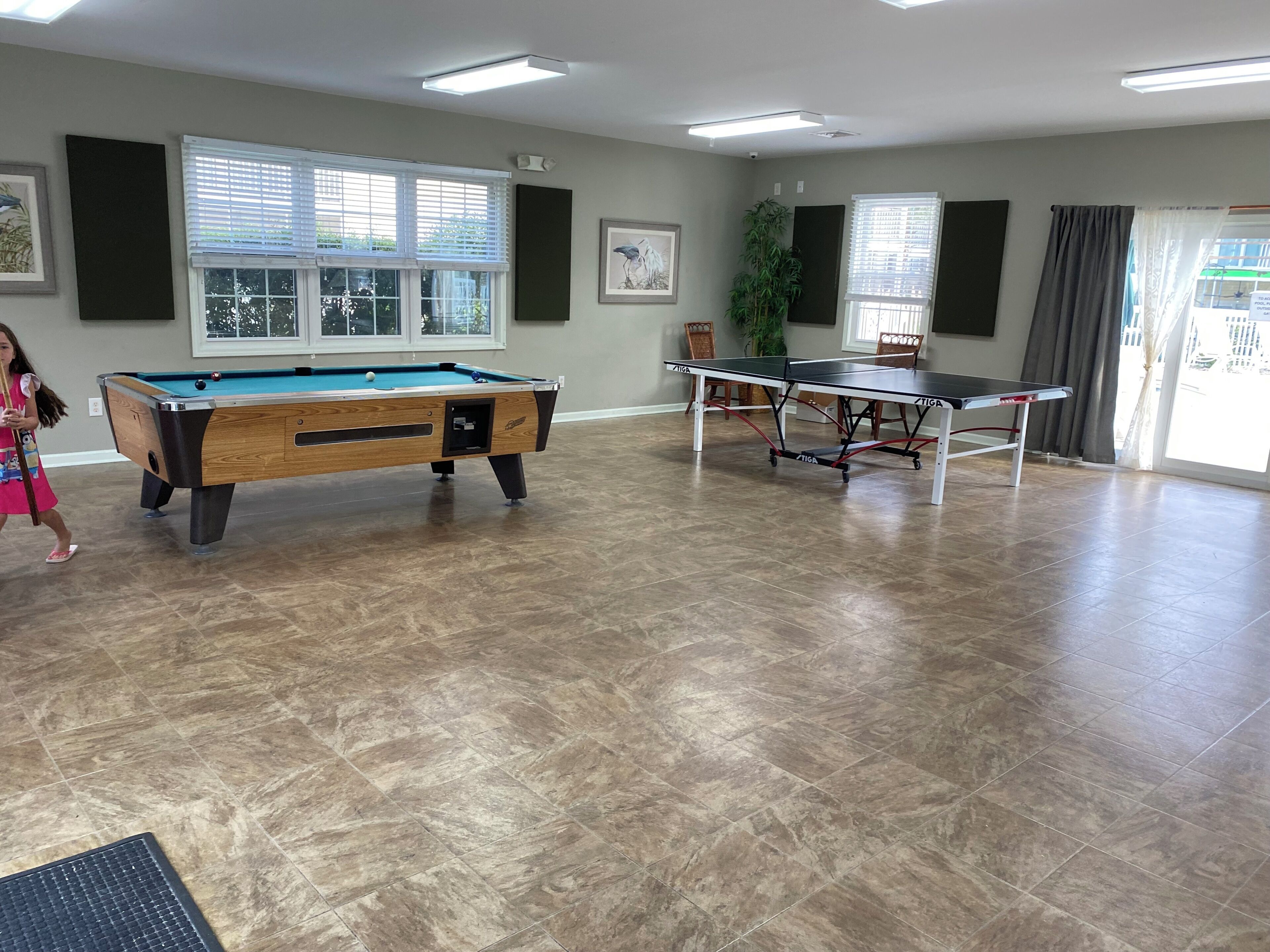 A pool table, ping pong table, and a billiards table in a room with large windows and a plant.