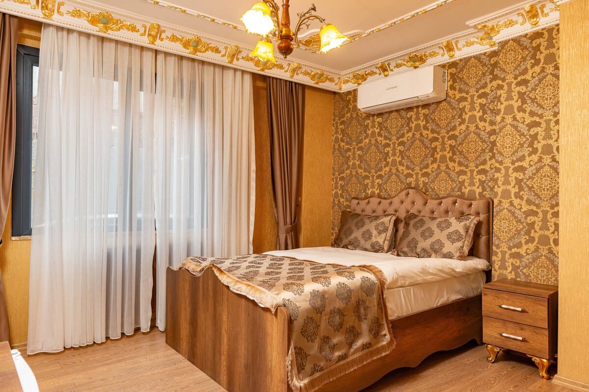 A bedroom with a bed, curtains, a nightstand, and an air conditioning unit.