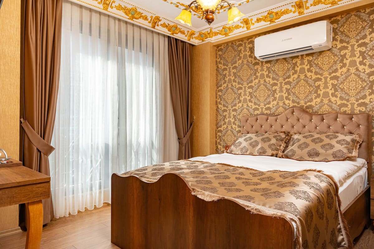 A bedroom with a wooden bed, a bedside table, a large window with curtains, an air conditioning unit, and a patterned wall.