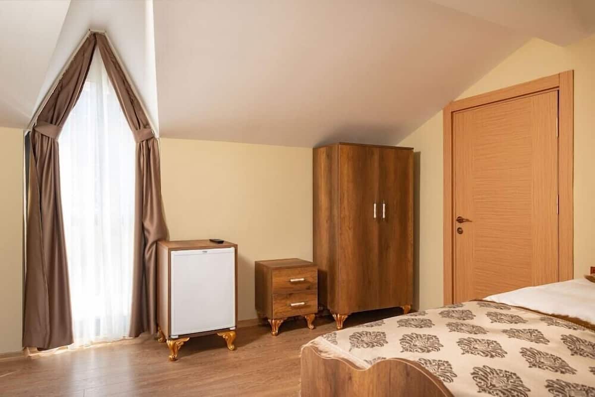 A bedroom with a bed, a wardrobe, a nightstand, and a small white appliance.