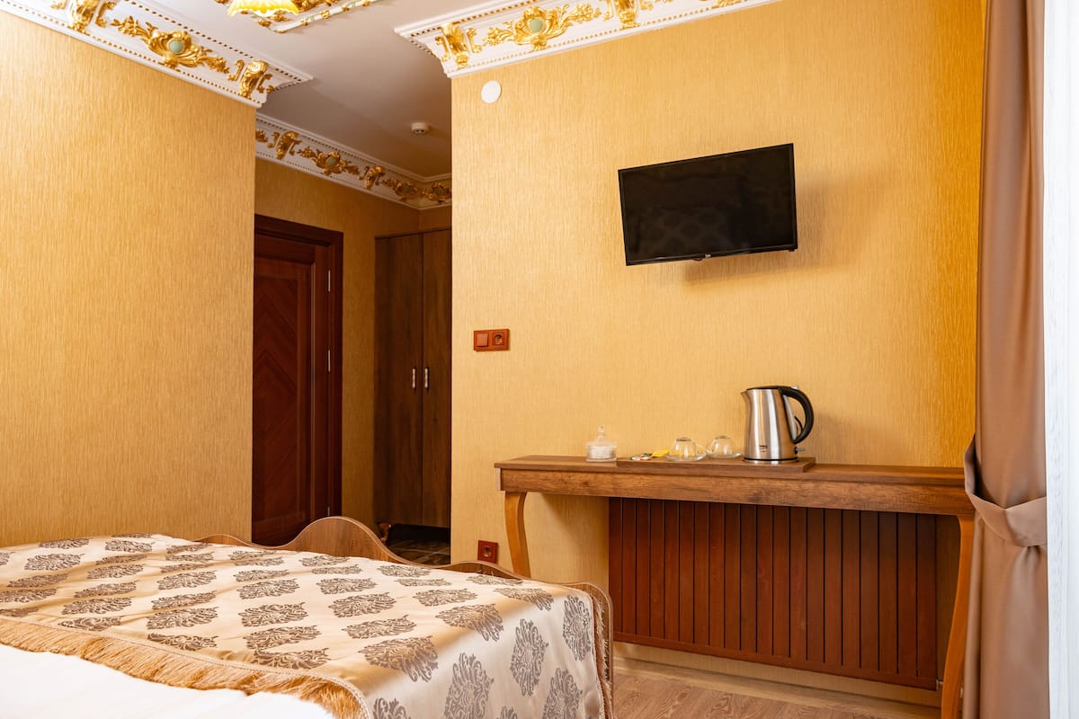 A hotel room with a bed, a wooden desk with a kettle, and a TV mounted on the wall.