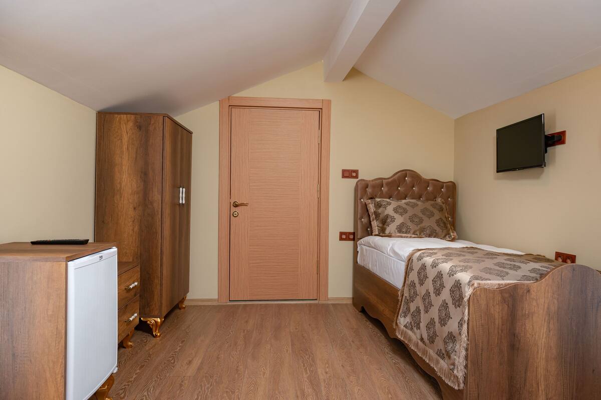 A bedroom with a wooden wardrobe, a bed with a patterned bedspread, and a mounted TV on the wall.